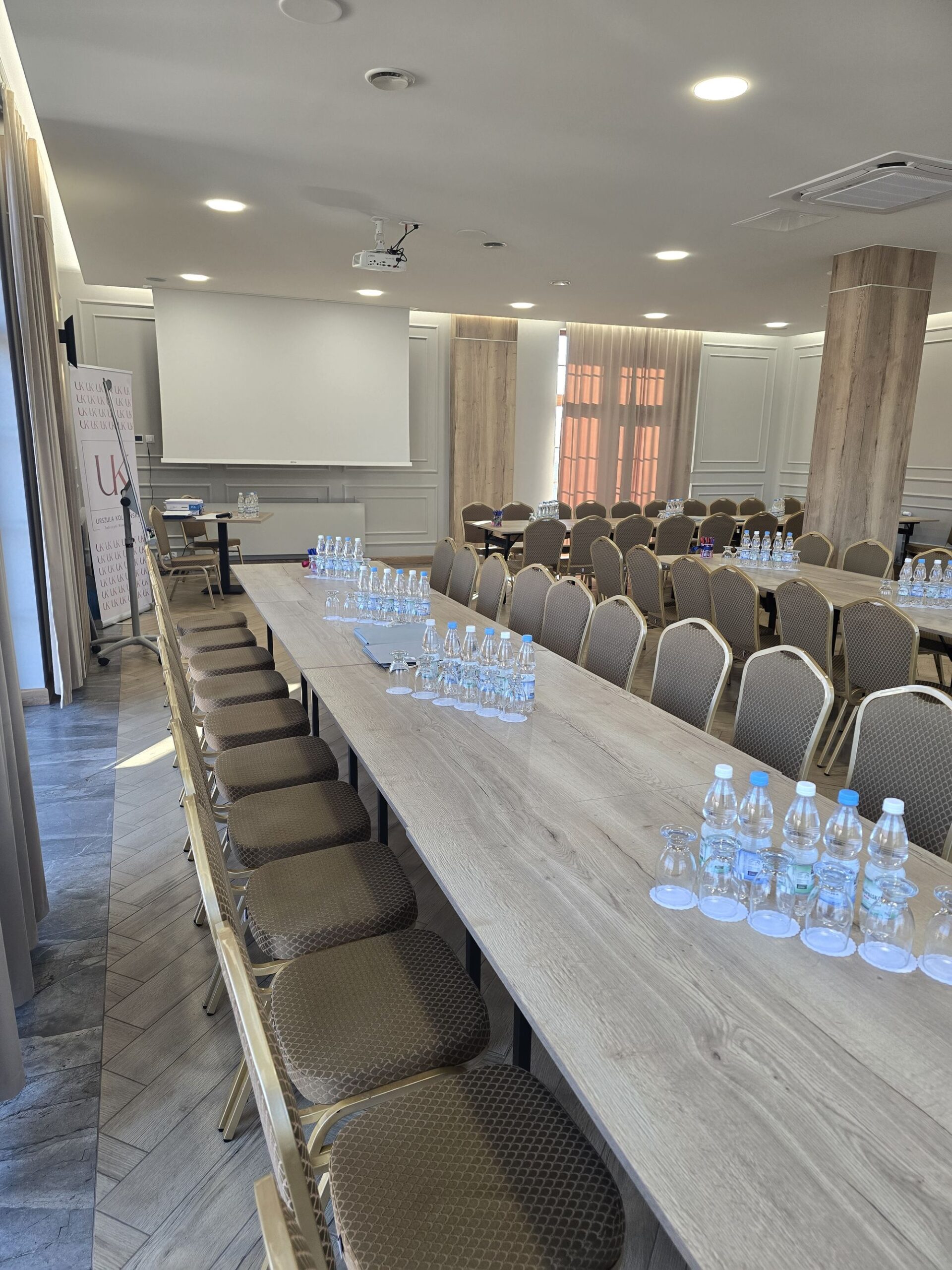 Długi drewniany stół konferencyjny z rządem brązowych krzeseł i butelkami wody ustawionymi do spotkania
