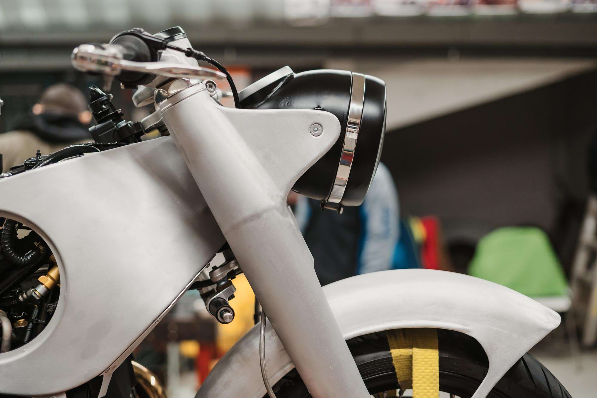 Przedni fragment surowo wykończonego motocykla z matowym białym błotnikiem, czarną okrągłą lampą i widocznym kołem
